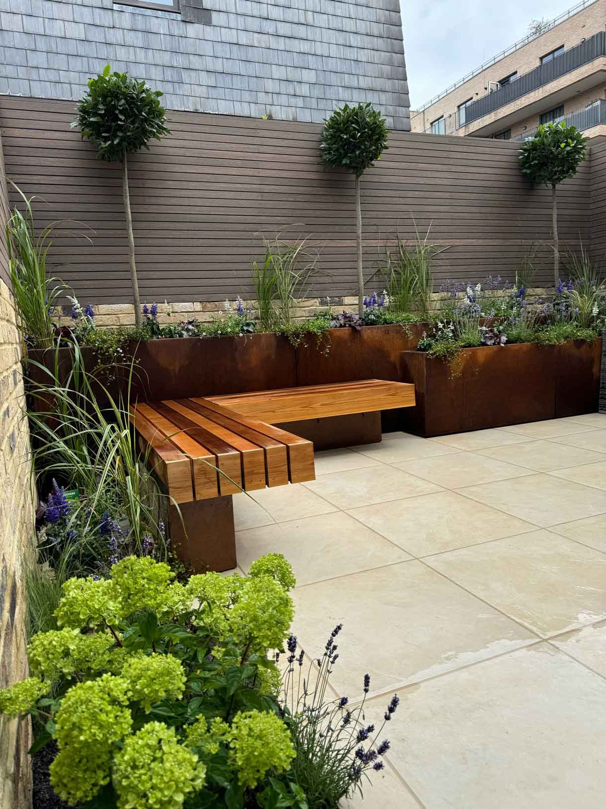Apartment courtyard garden with corten steel planters, stone paving and hardwood bench seating