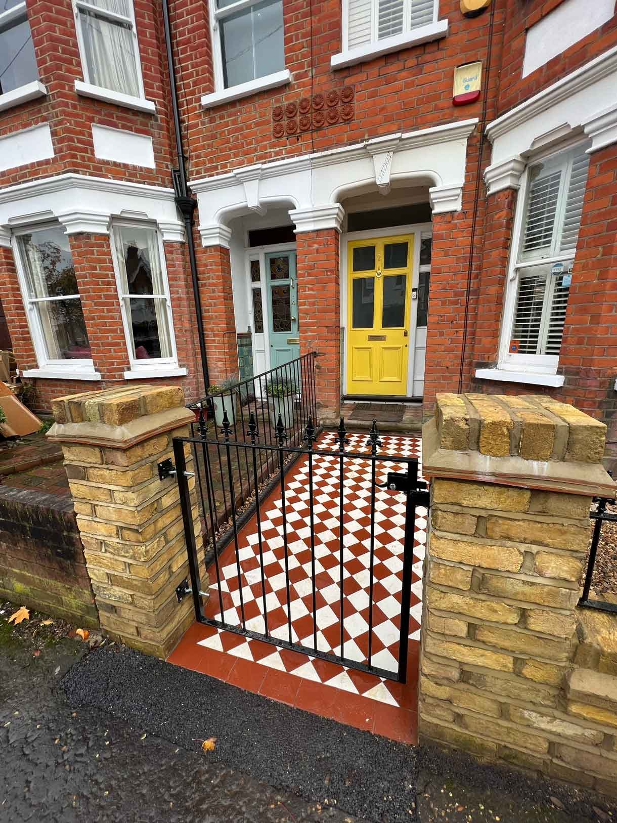 A yellow brick wall and a red and white victorian path in checkerboard style.