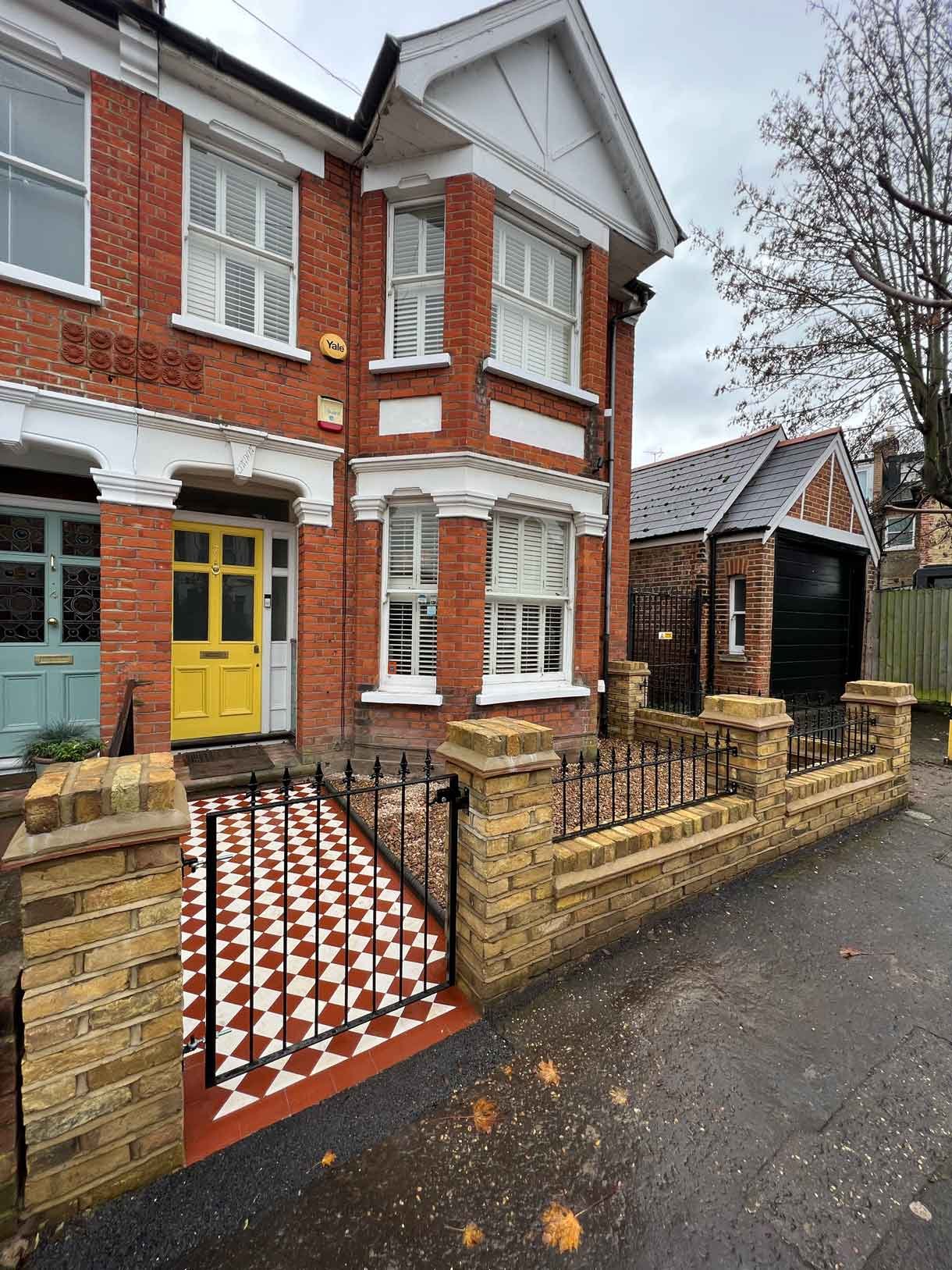 A yellow brick wall and a red and white victorian path in checkerboard style.