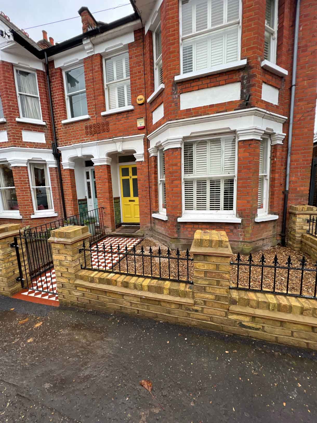 A yellow brick wall and a red and white victorian path in checkerboard style.