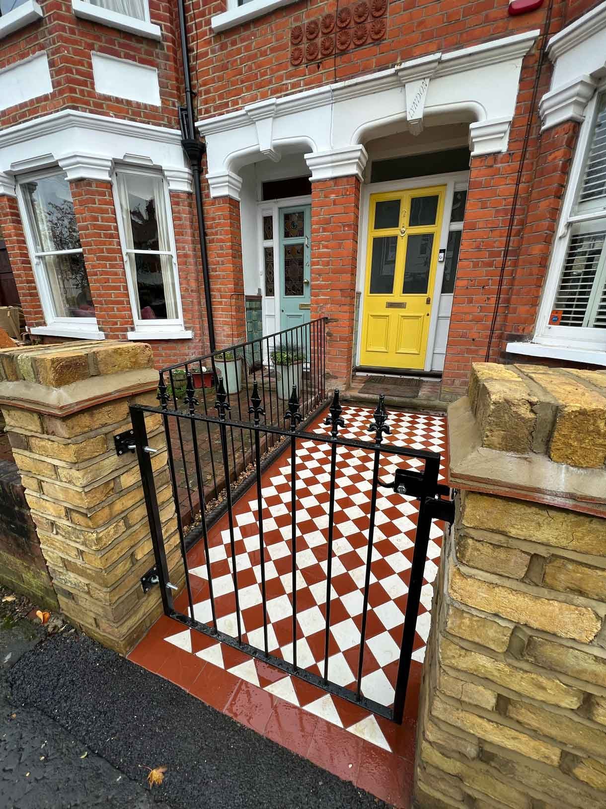 A yellow brick wall and a red and white victorian path in checkerboard style.