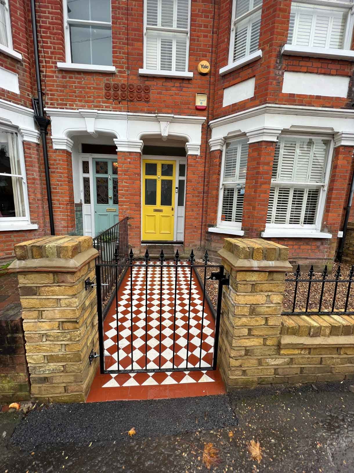 A yellow brick wall and a red and white victorian path in checkerboard style.