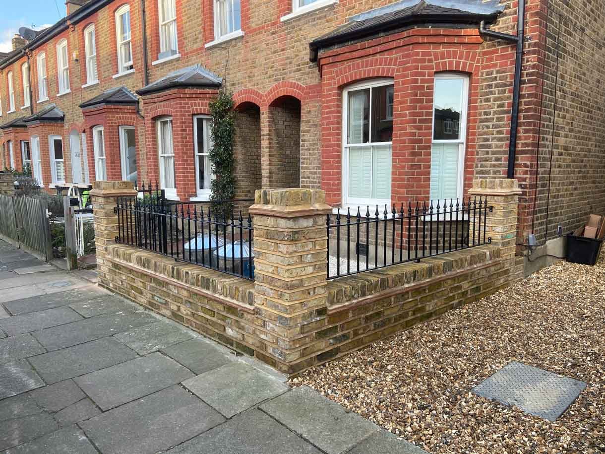 Brick wall using London stock yellow bricks with railings on top and a gate.
