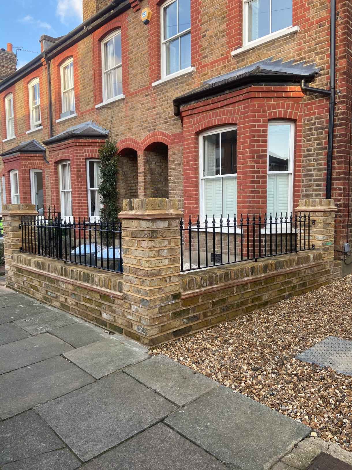 Brick wall using London stock yellow bricks with railings on top and a gate.