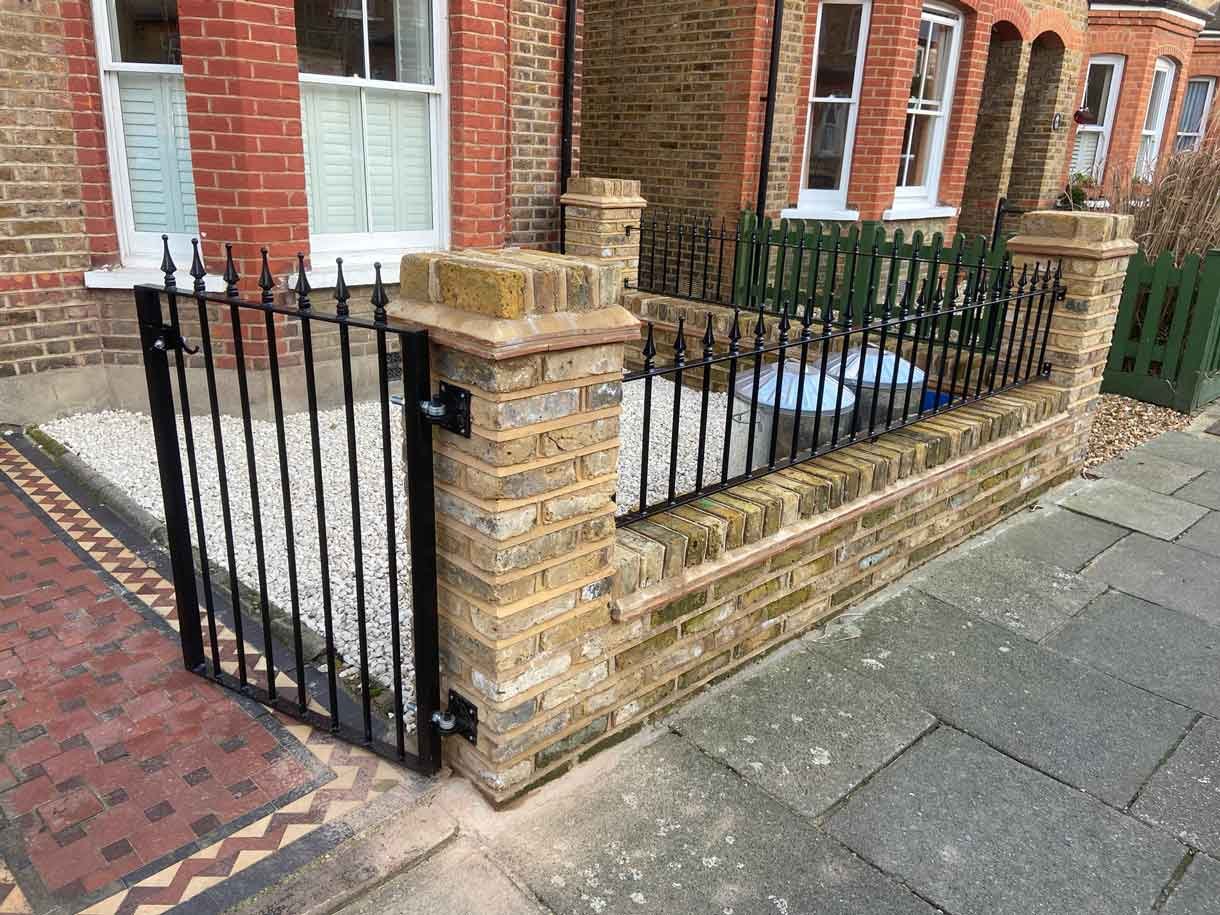 Brick wall using London stock yellow bricks with railings on top and a gate.