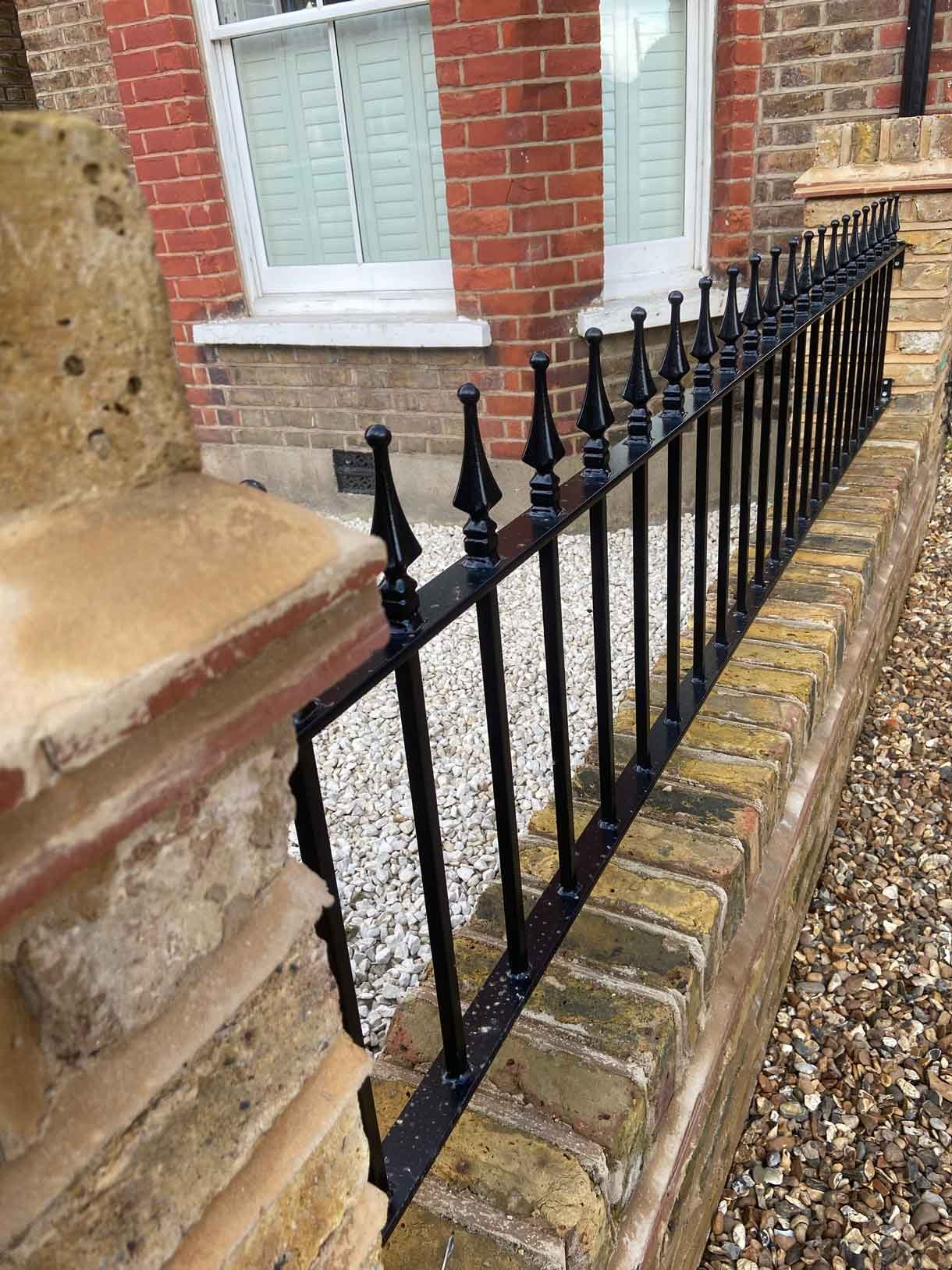 Brick wall using London stock yellow bricks with railings on top and a gate.