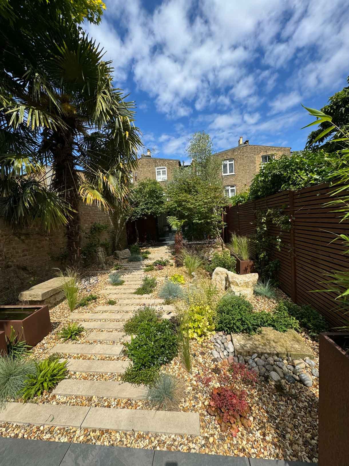 A gravel garden with plants and boulders, a water feature and stepping stones.