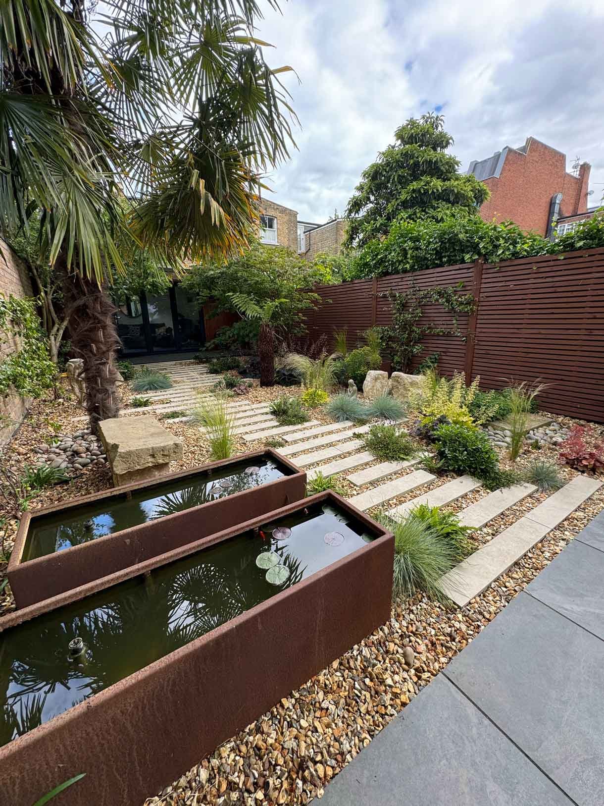 A gravel garden with plants and boulders, a water feature and stepping stones.