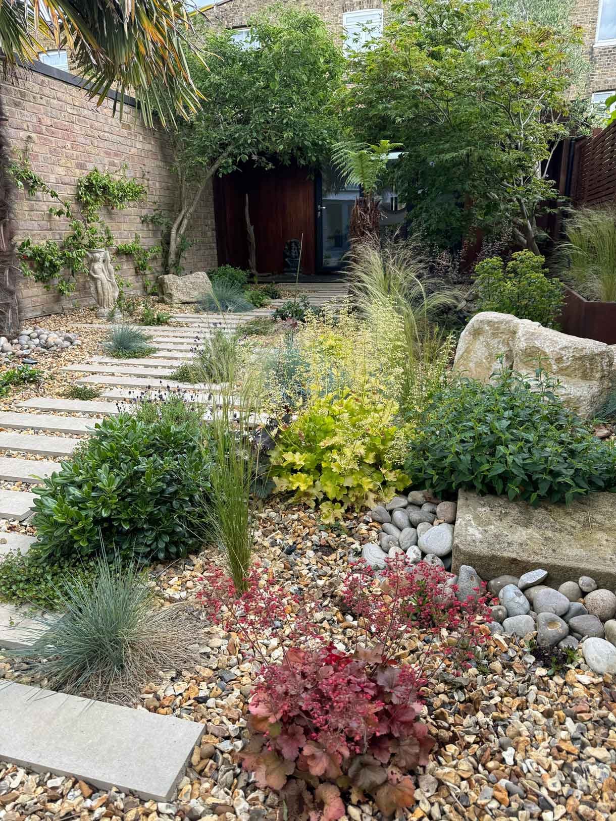 A gravel garden with plants and boulders, a water feature and stepping stones.