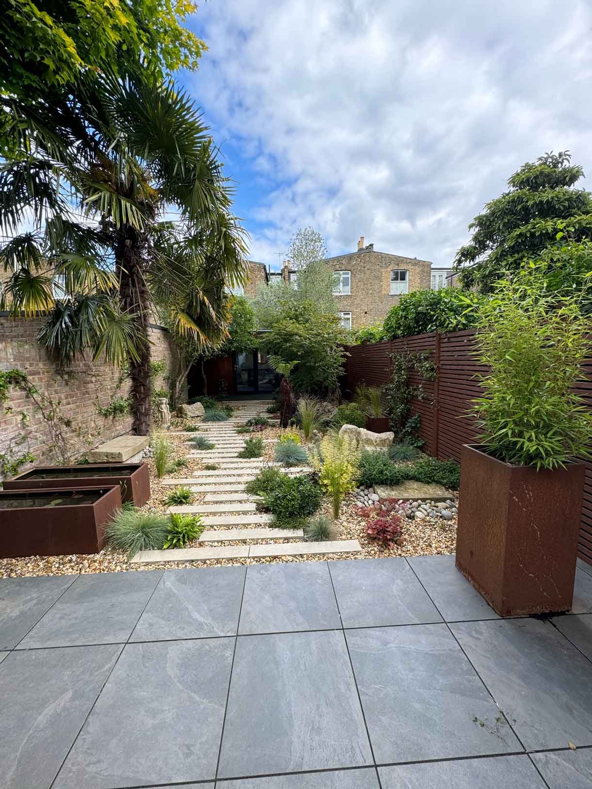 A gravel garden with plants and boulders, a water feature and stepping stones.