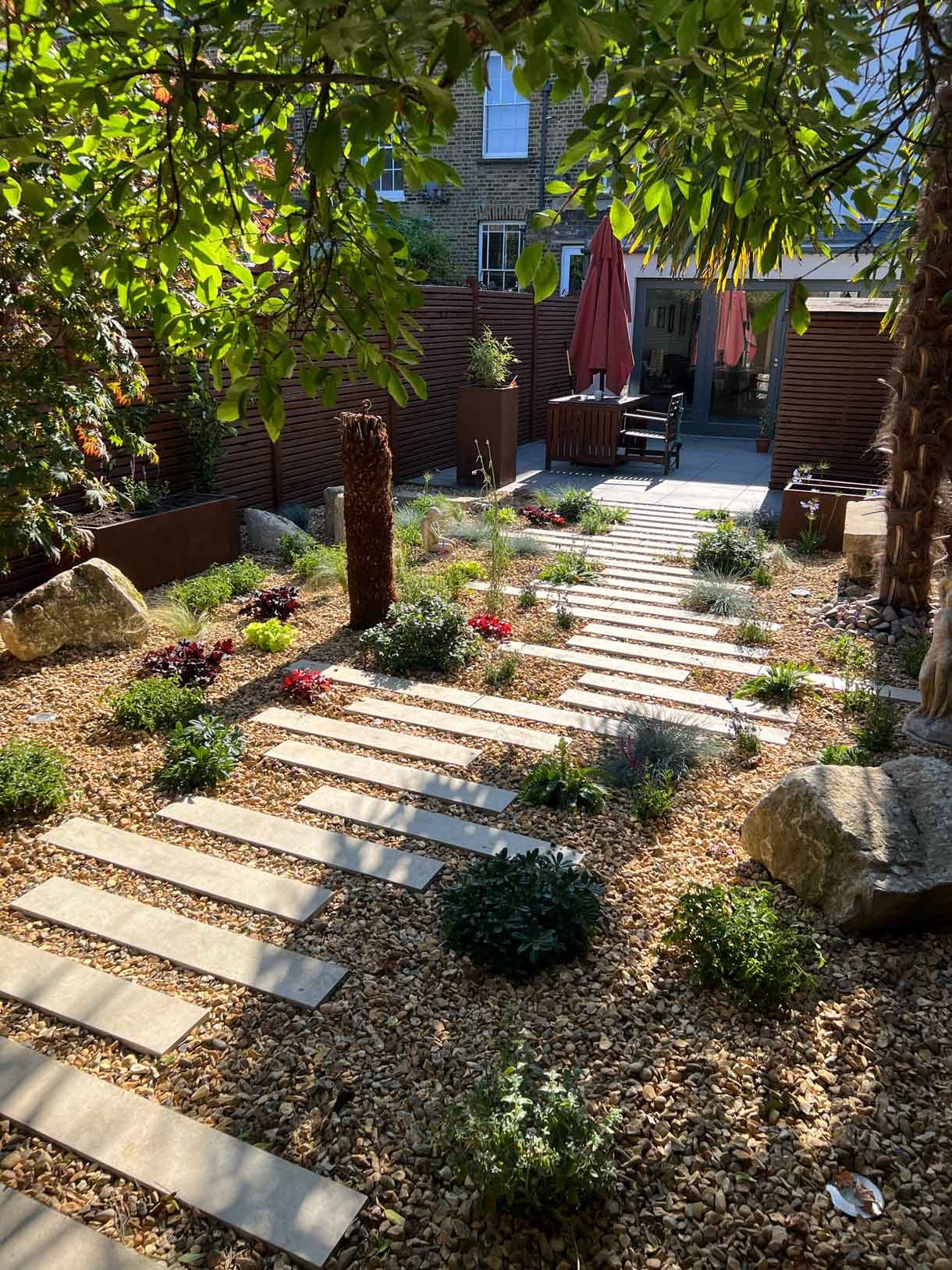 A gravel garden with plants and boulders, a water feature and stepping stones.