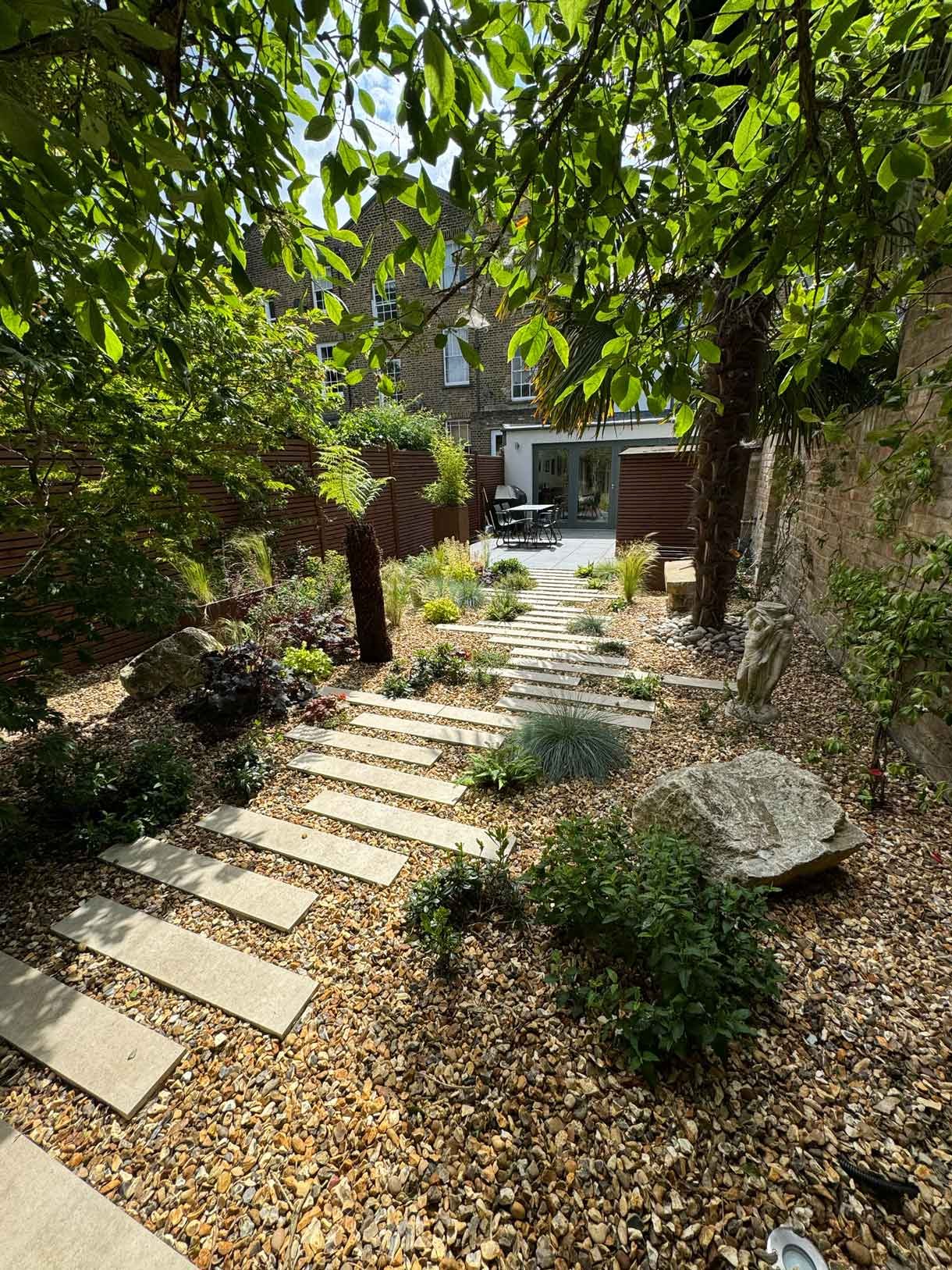 A gravel garden with plants and boulders, a water feature and stepping stones.