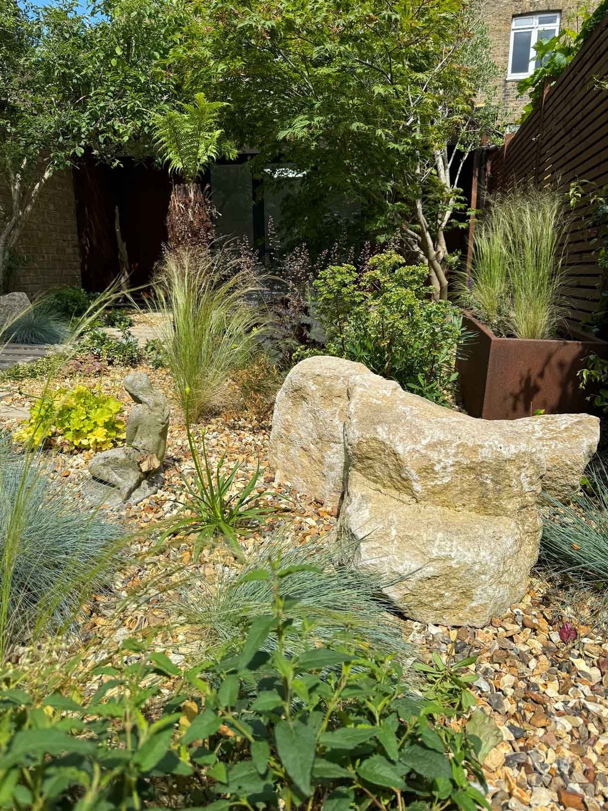 A gravel garden with plants and boulders, a water feature and stepping stones.