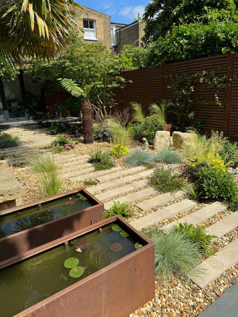 A gravel garden with plants and boulders, a water feature and stepping stones.