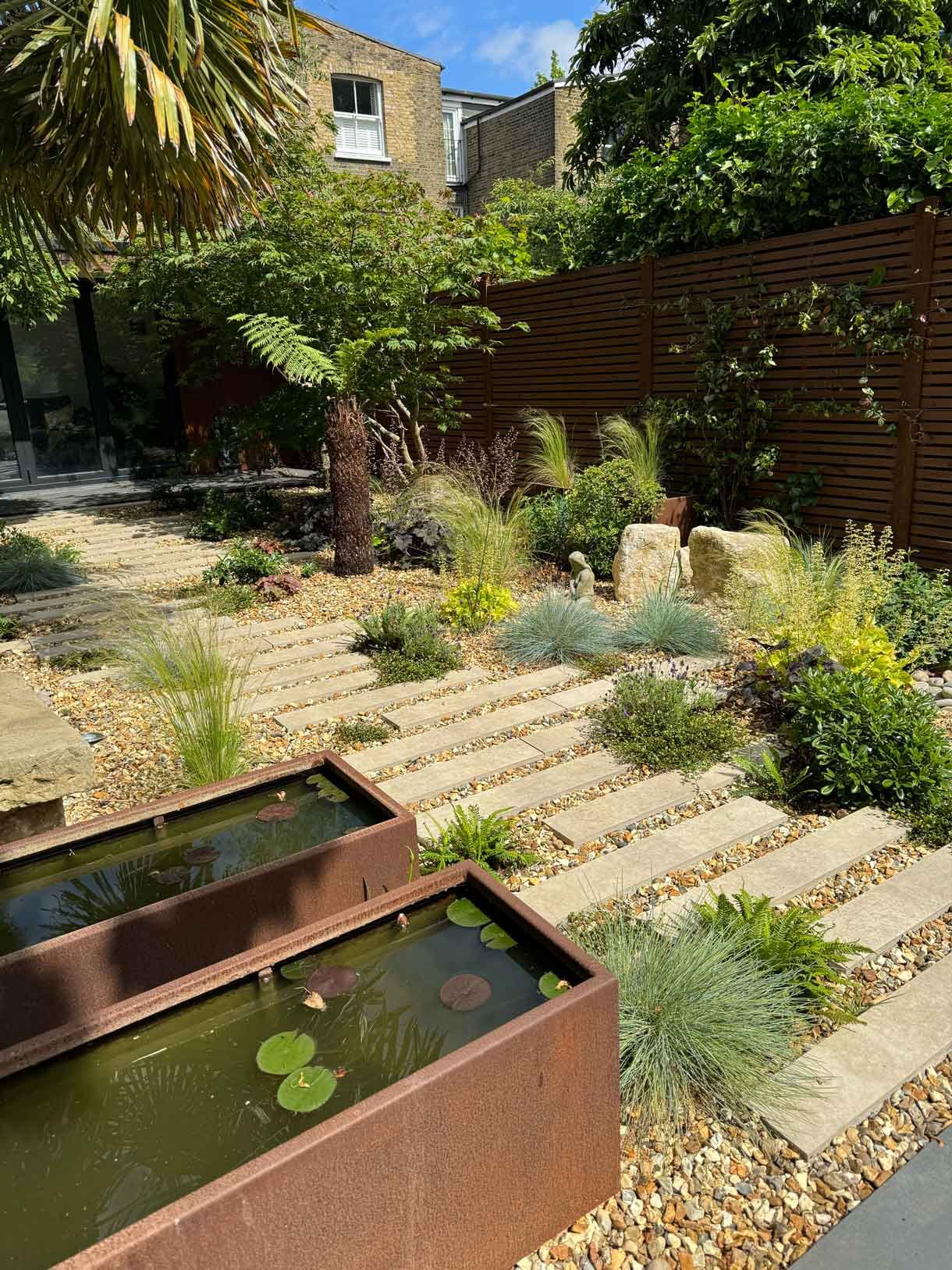 A gravel garden with plants and boulders, a water feature and stepping stones.