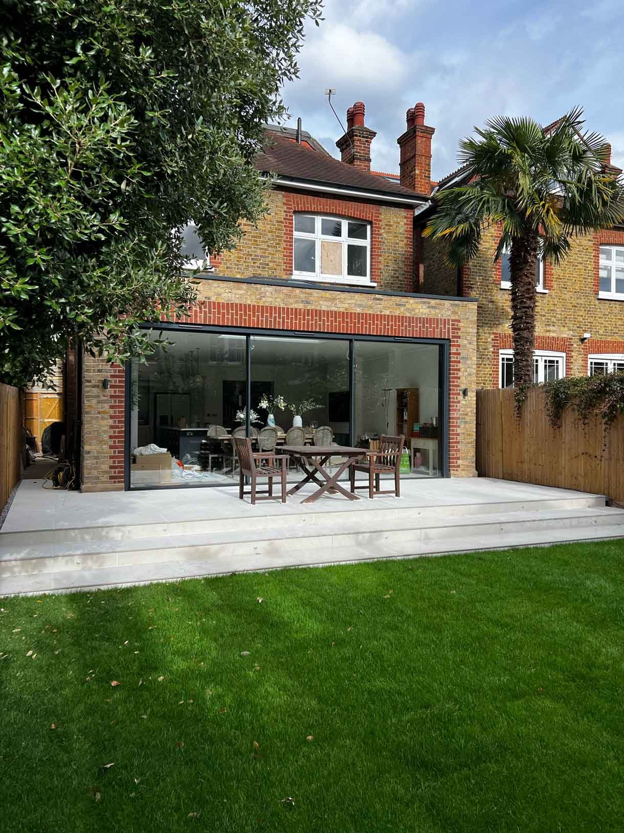 A raised patio of a new brick extension in Putney, London complete with green lawn.