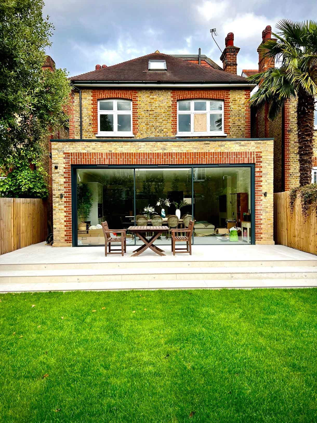 A raised patio of a new brick extension in Putney, London complete with green lawn.