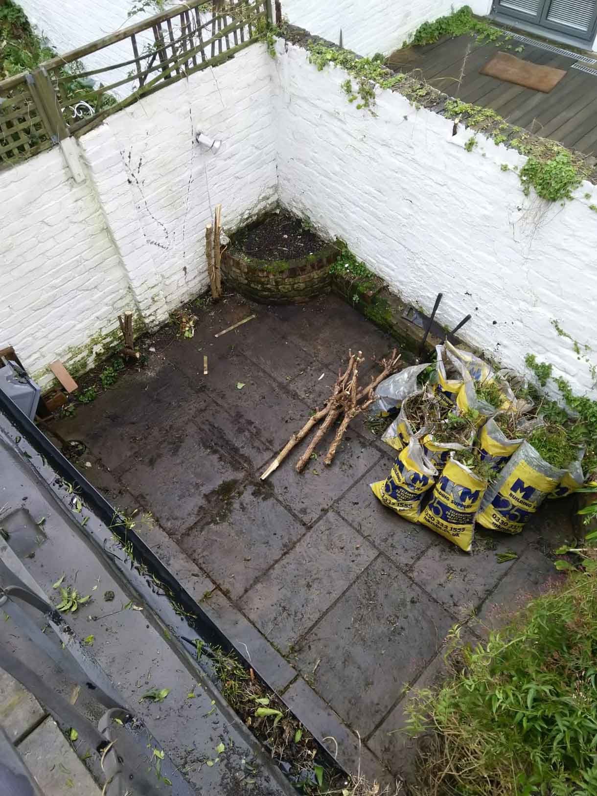 An image of the property with weeds in the courtyard garden with a white brick wall.
