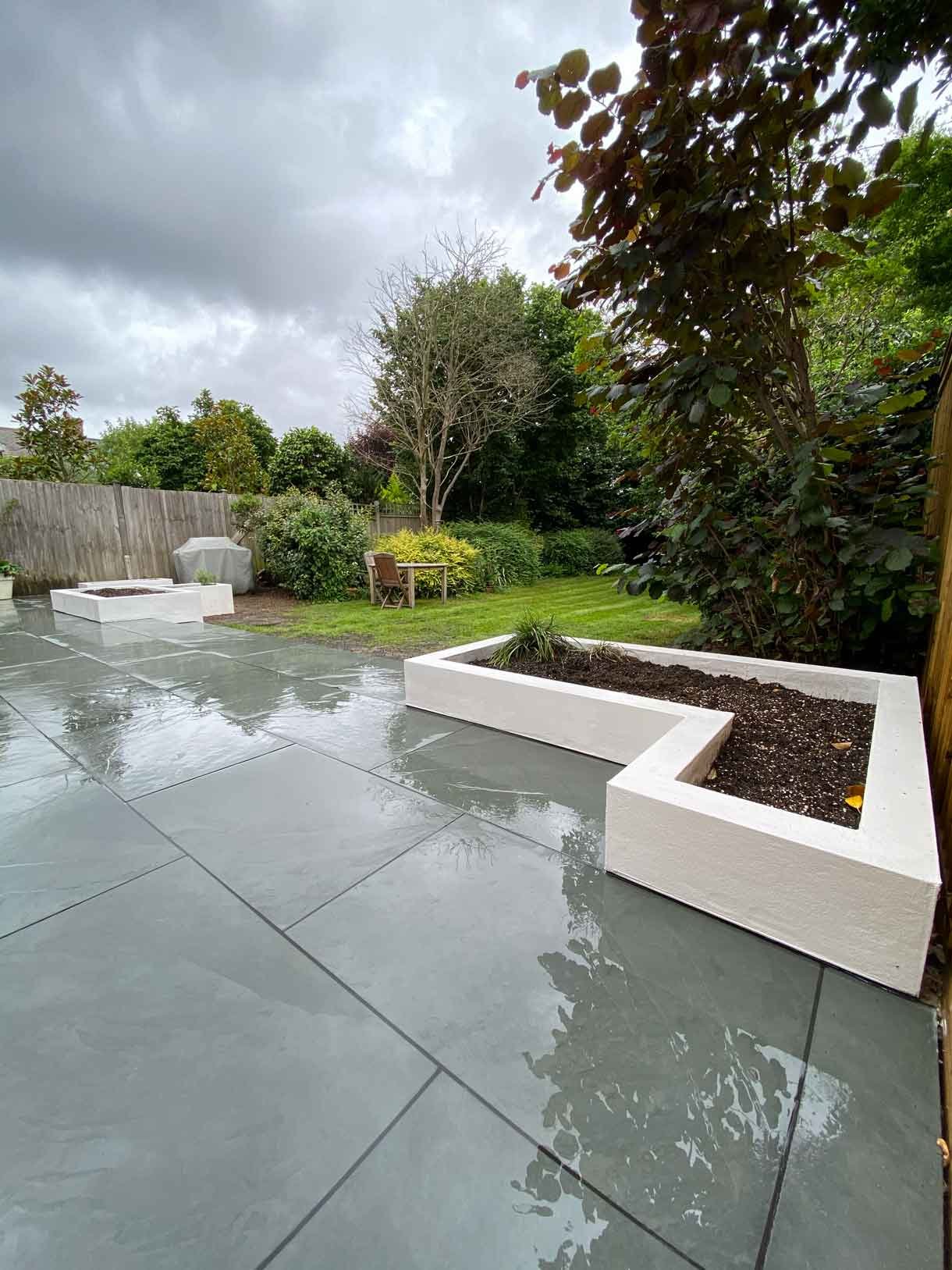 A raised grey slate patio in Teddington, with white rendered planters.
