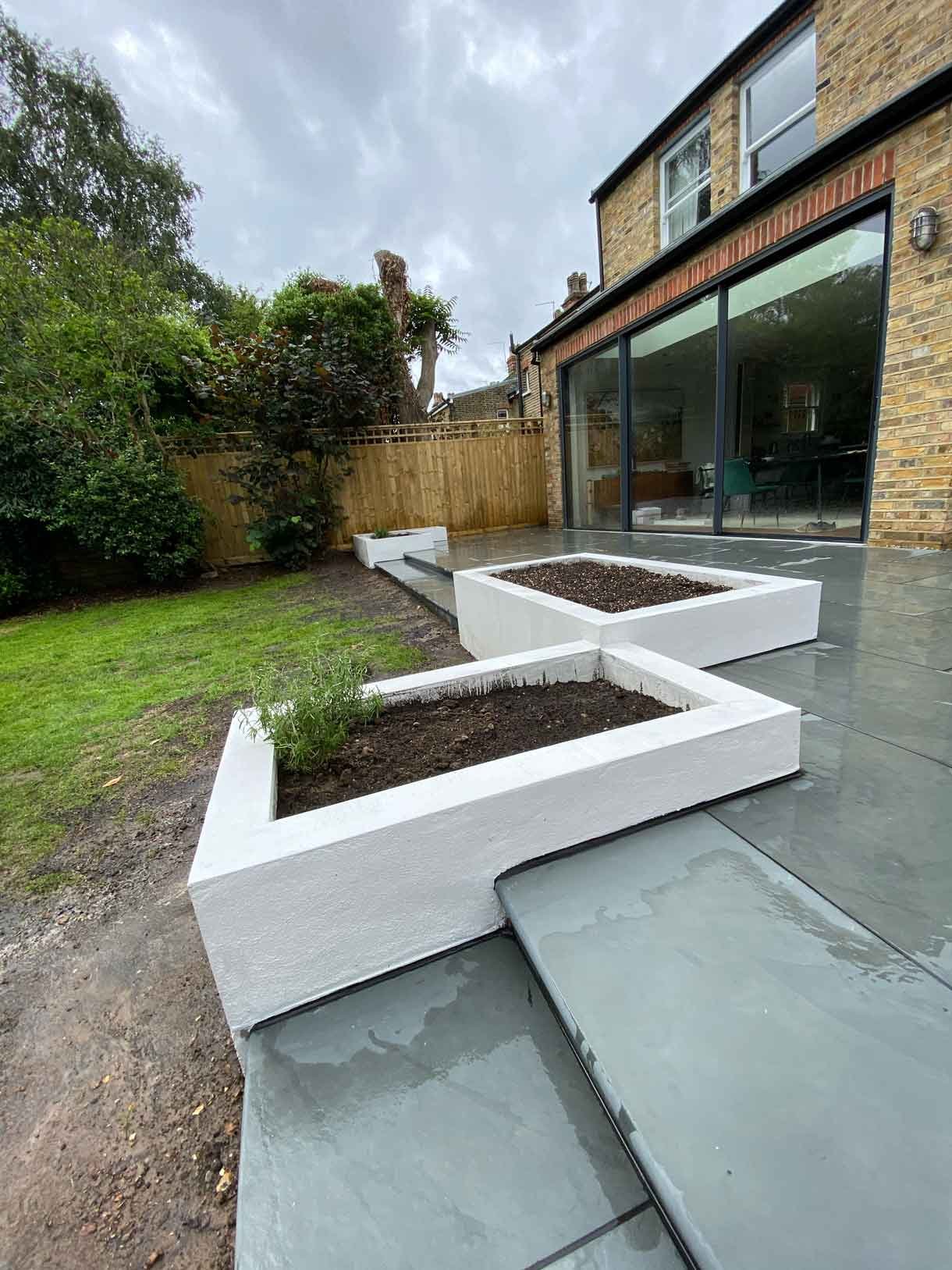 A raised grey slate patio in Teddington, with white rendered planters.