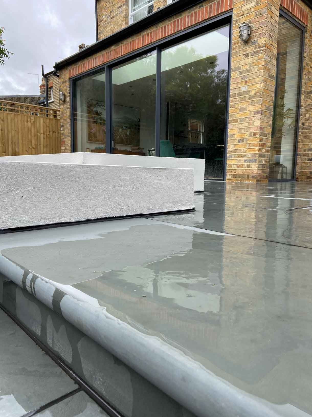 A raised grey slate patio in Teddington, with white rendered planters.