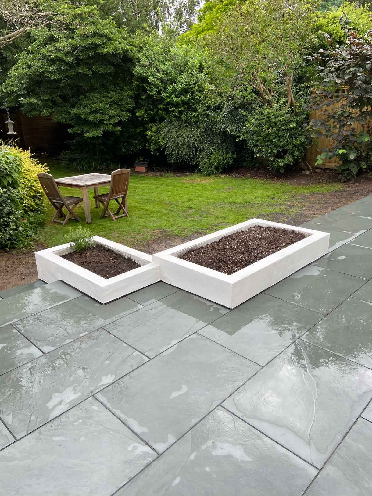 A raised grey slate patio in Teddington, with white rendered planters.