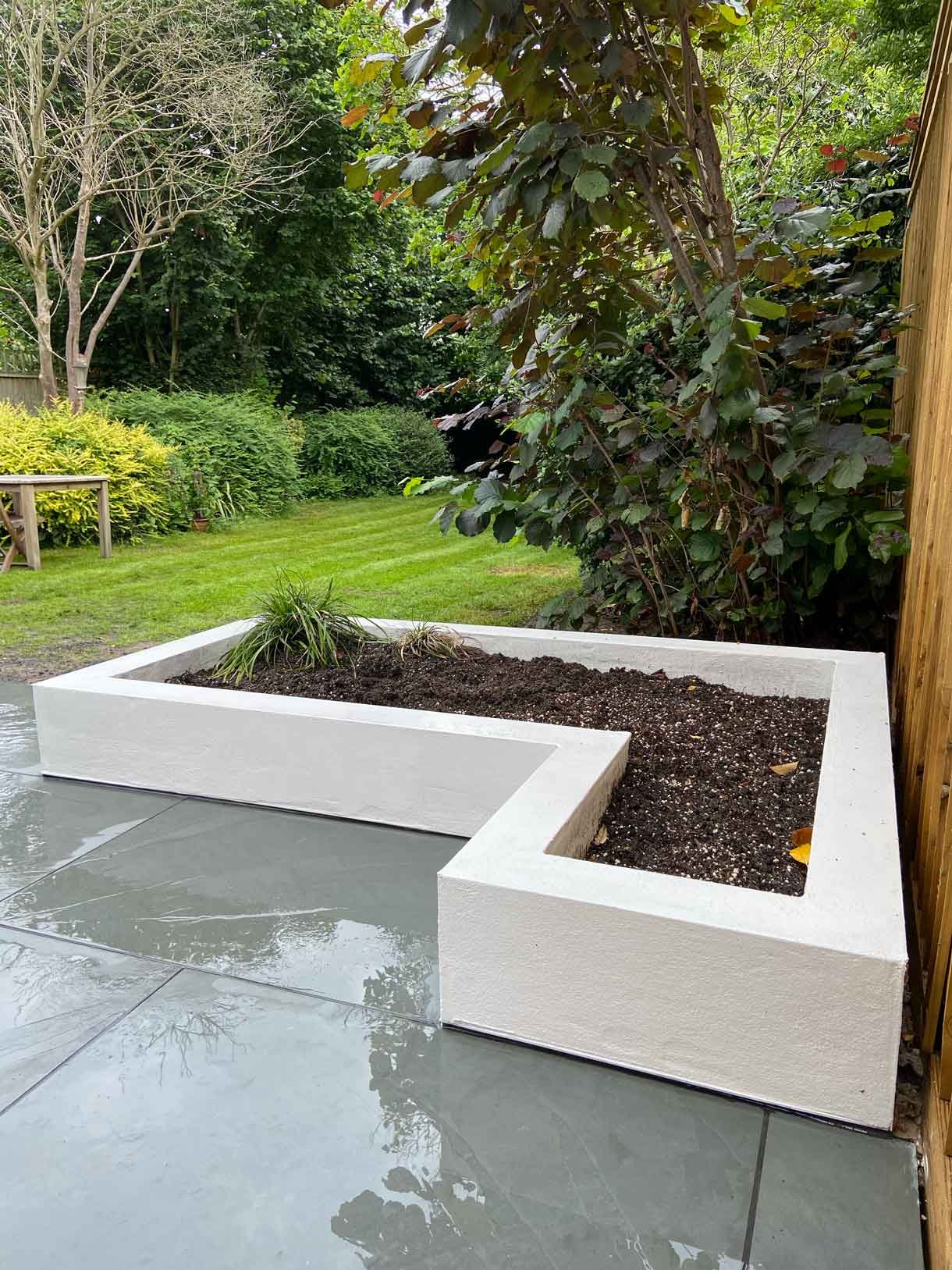 A raised grey slate patio in Teddington, with white rendered planters.