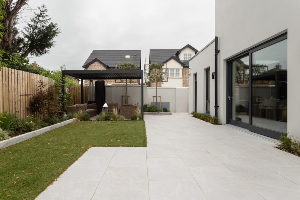 Modern new-build house rear garden with porcelain paving, lawn, pergola and bifold doors